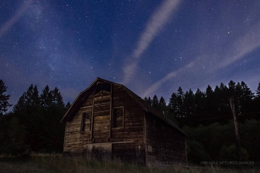 A wood barn stands against a dark sky with trees at night
