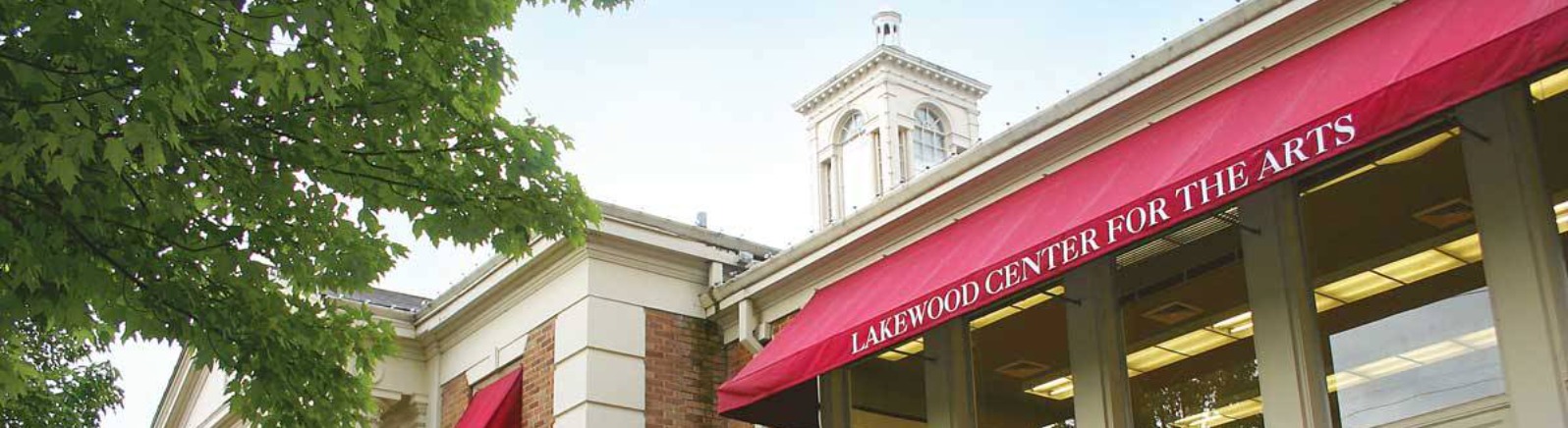 Exterior view of the Lakewood Center for the Arts, featuring large windows, red awnings, and vibrant flower beds. Lush greenery surrounds the building.