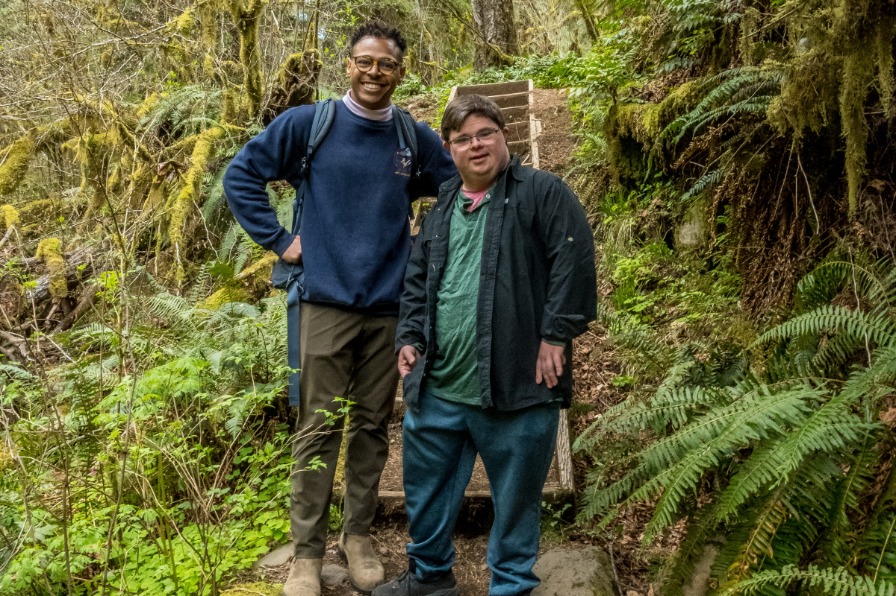 A guided hike with Mt. Hood Outfitters Two hikers pose on a dirt trail surrounded by green trees.
