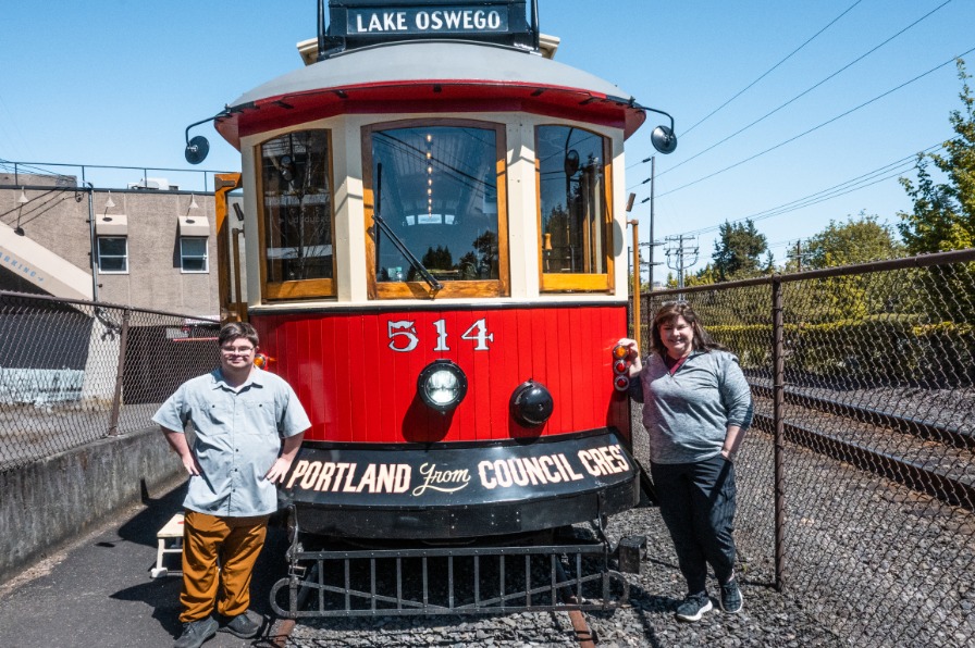 Two people stand next to a historic red trolley