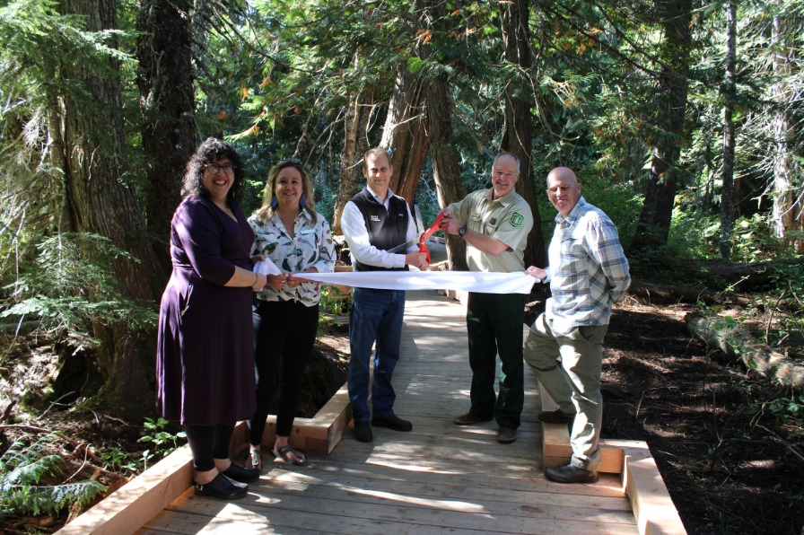 The Trillium Lake boardwalk A group of people cut a white ribbon with large scissors over a new boardwalk