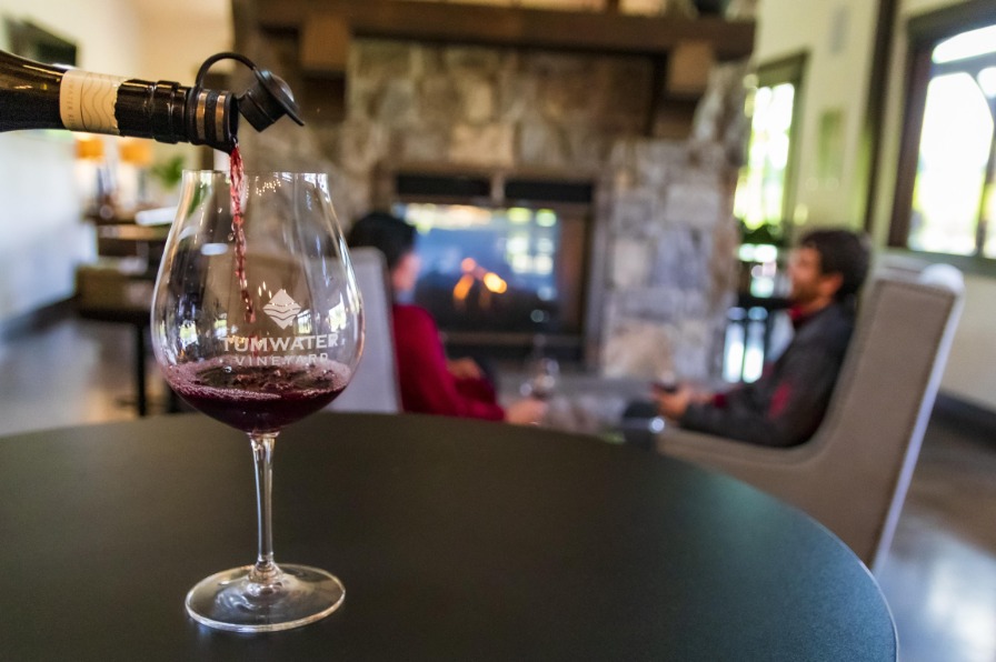 Red wine pouring in a glass with people in the background seated next to a fireplace
