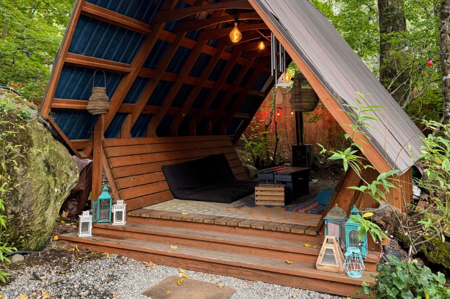 A wood a-frame building covers a table surrounded by trees
