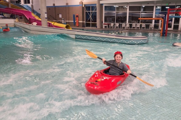 Child smiles in a kayak in an indoor pool