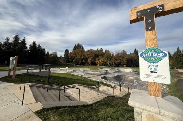 Skate park with smooth concrete ramps and bowls, surrounded by trees. A sign labeled "Base Camp" indicates the ascent path.