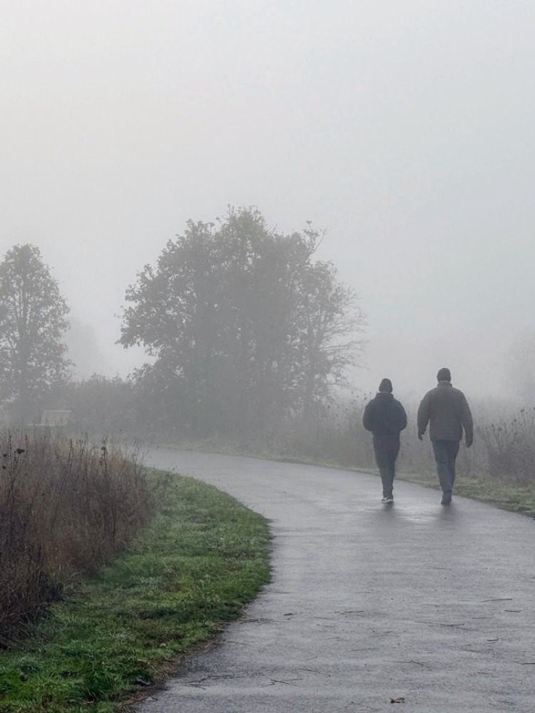 Two people walk on a paved trail in the fog.