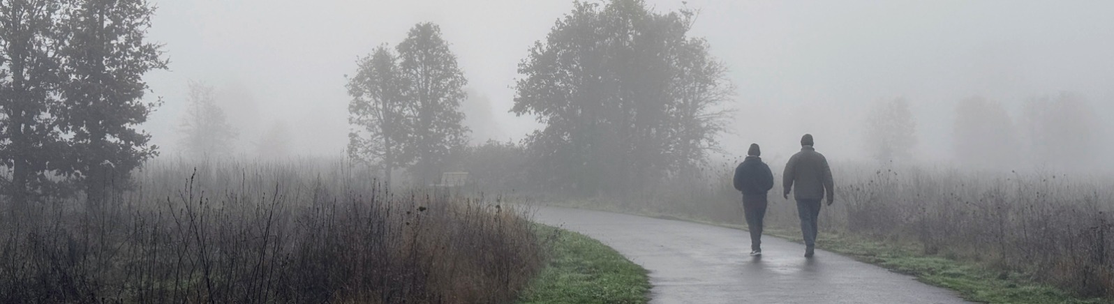 Two people walk on a paved trail in the fog.
