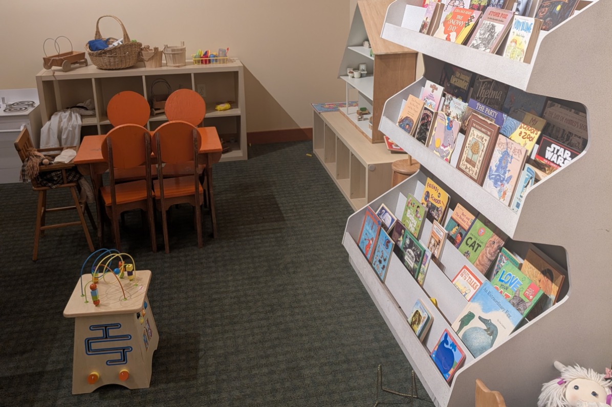 A rack of books stands along a tiny orange table for kids.
