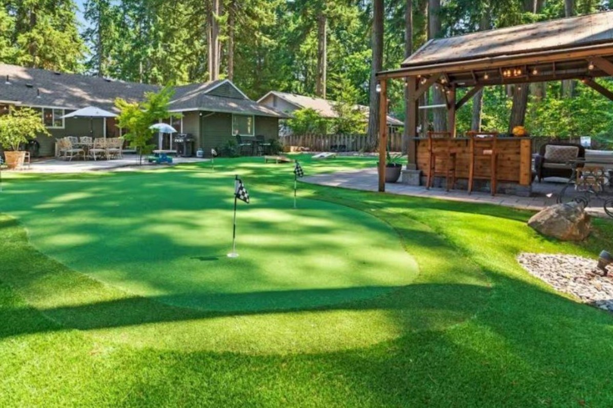 A lush backyard features a green with flags, surrounded by tall trees and a cozy gazebo.