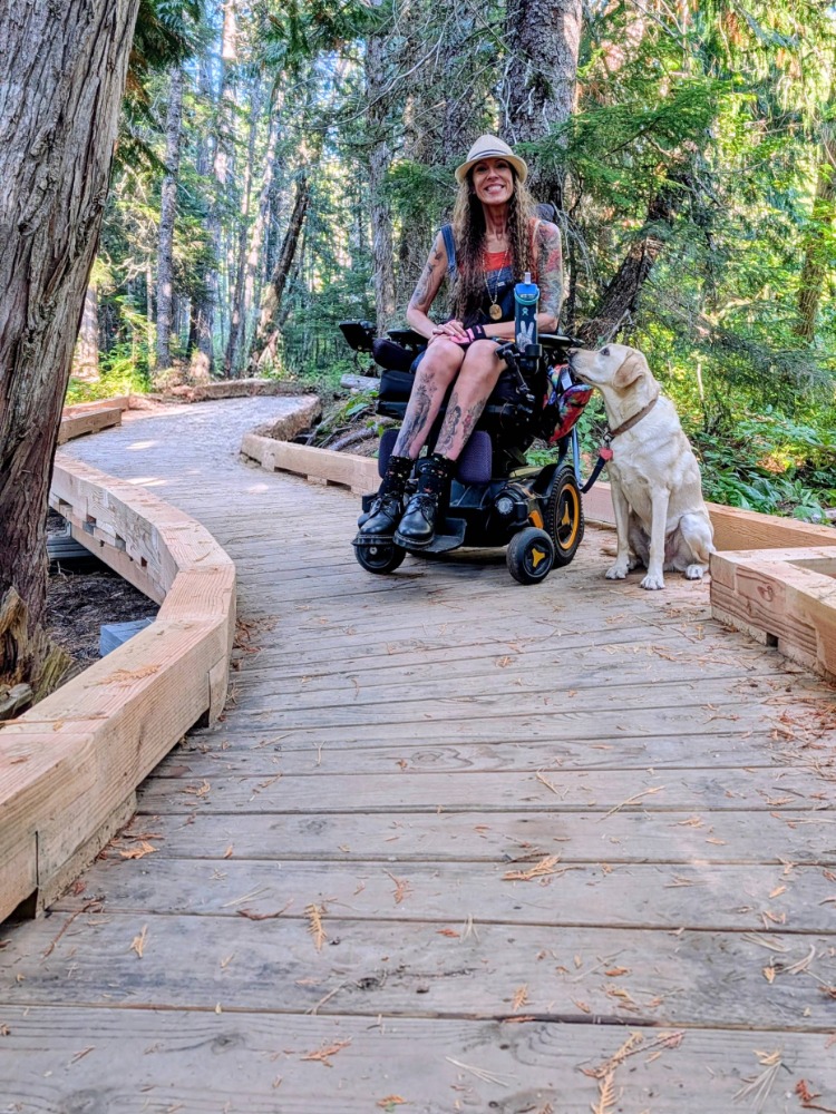 A wheelchair user goes along a boardwalk surrounded by green trees