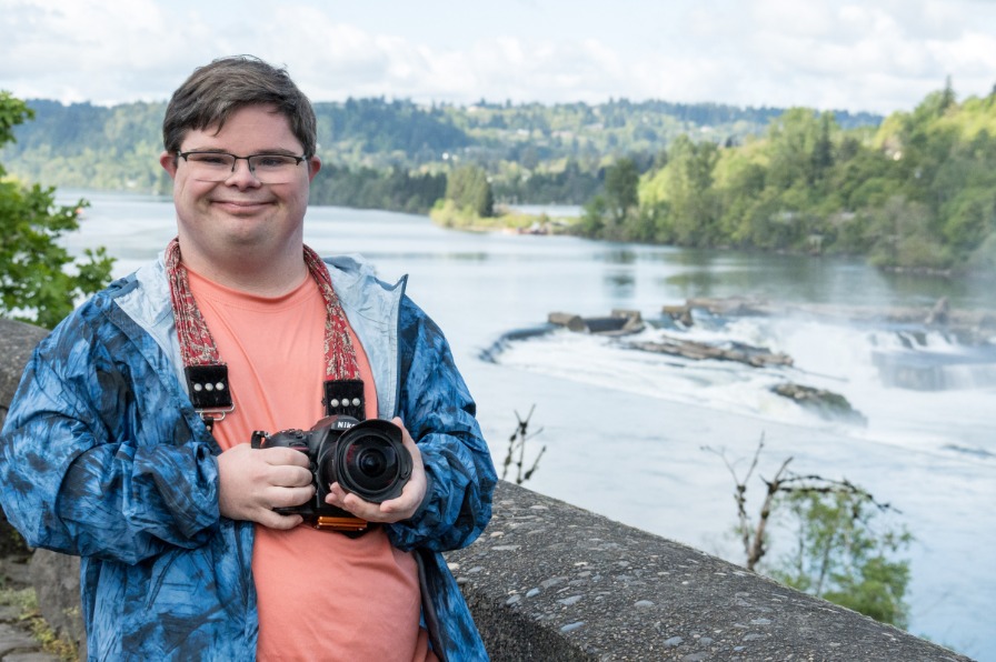 A person with a camera poses at a waterfall