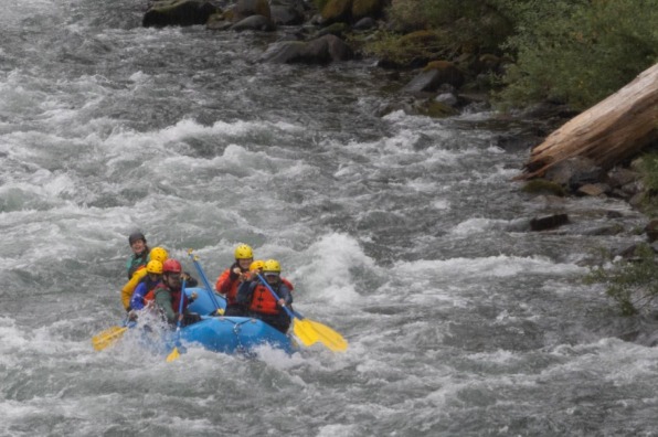 Rafters in yellow helmets paddle a blue raft through white water rapids on the Clackamas River