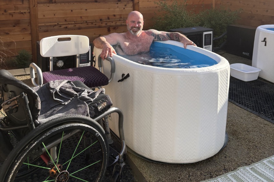 A person sits in a hot tub next to a wheelchair.