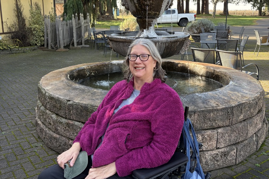 Person in a wheel chair smiles in front of an outdoor fountain.
