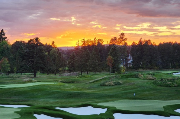 A scenic golf course at sunset, featuring lush green fairways, sand traps, and a vibrant sky with hues of orange and purple.