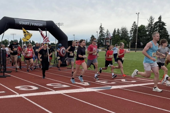 Runners in athletic gear sprinting on a track, passing under a "START/FINISH" arch. Flags and trees line the background.