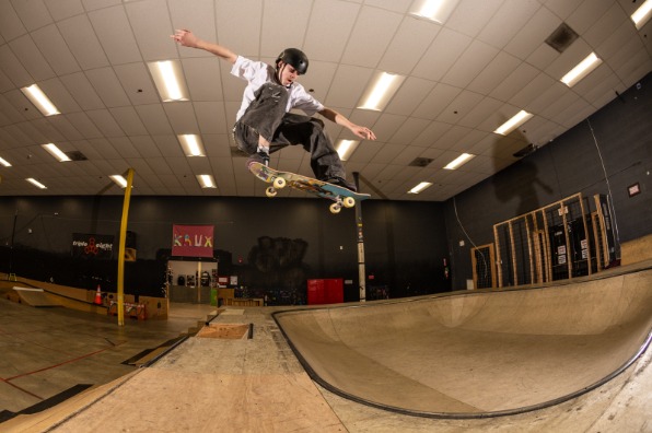 A skateboarder performs an aerial trick in a well-lit indoor skate park, featuring ramps and various obstacles.