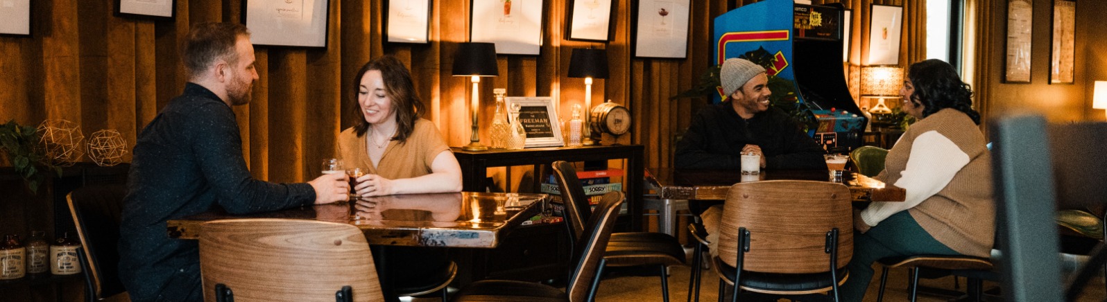 A cozy bar scene featuring people engaged in conversation. Warm lighting and art on the walls enhance the atmosphere.