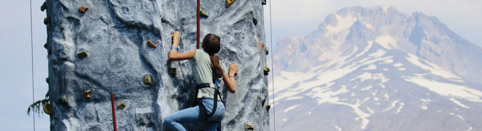 A person climbs a fake rock wall with Mt. Hood in the background