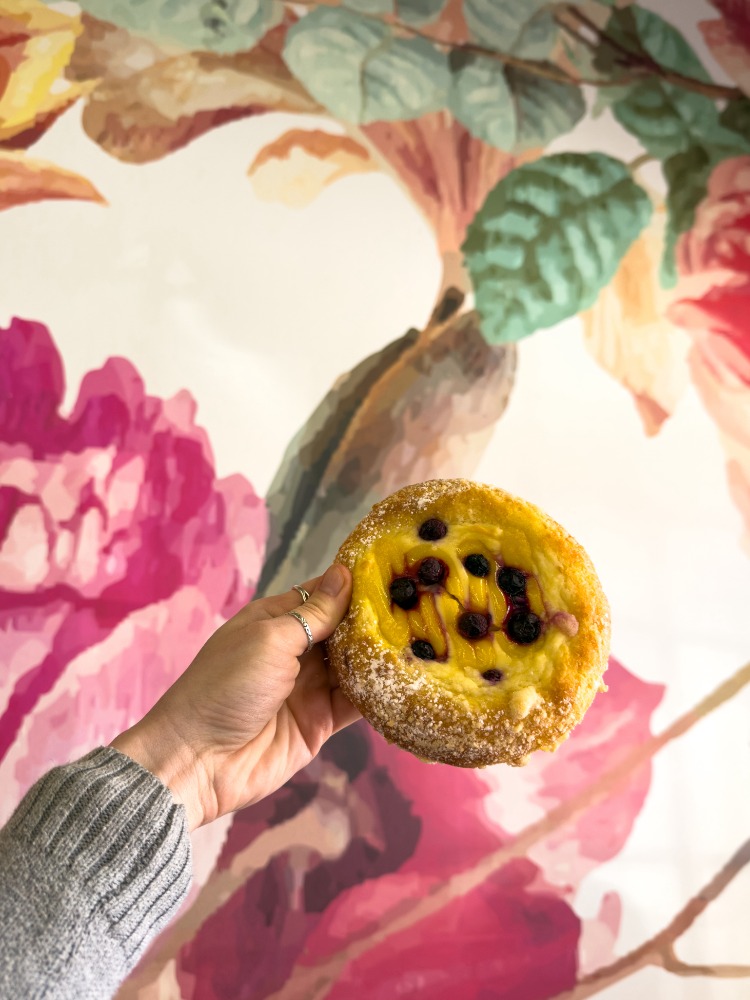 Hand holding up a pastry against floral wallpaper