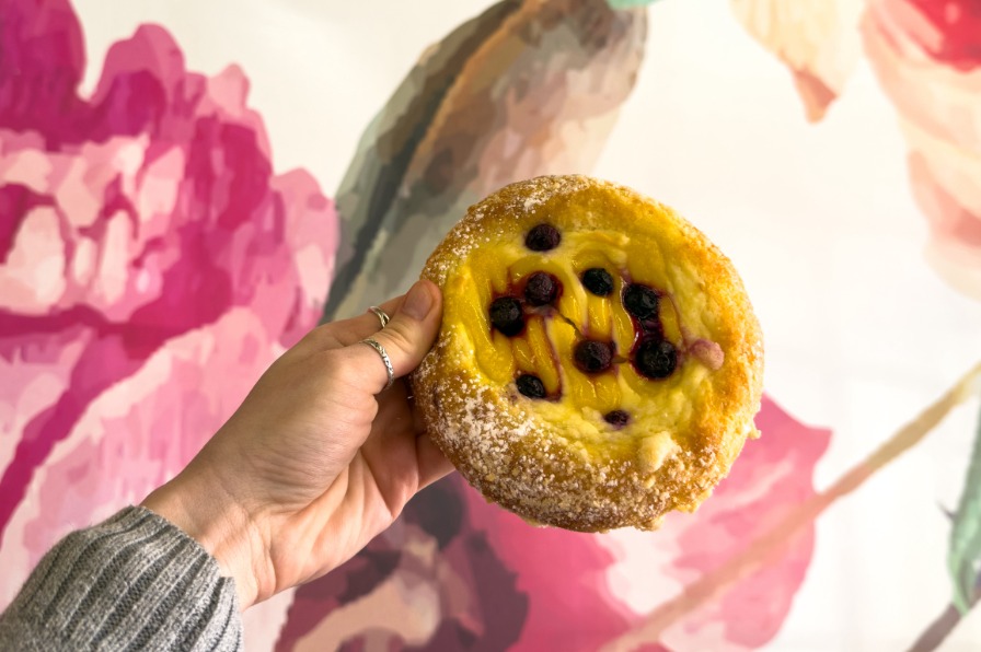 Hand holding up a pastry against floral wallpaper