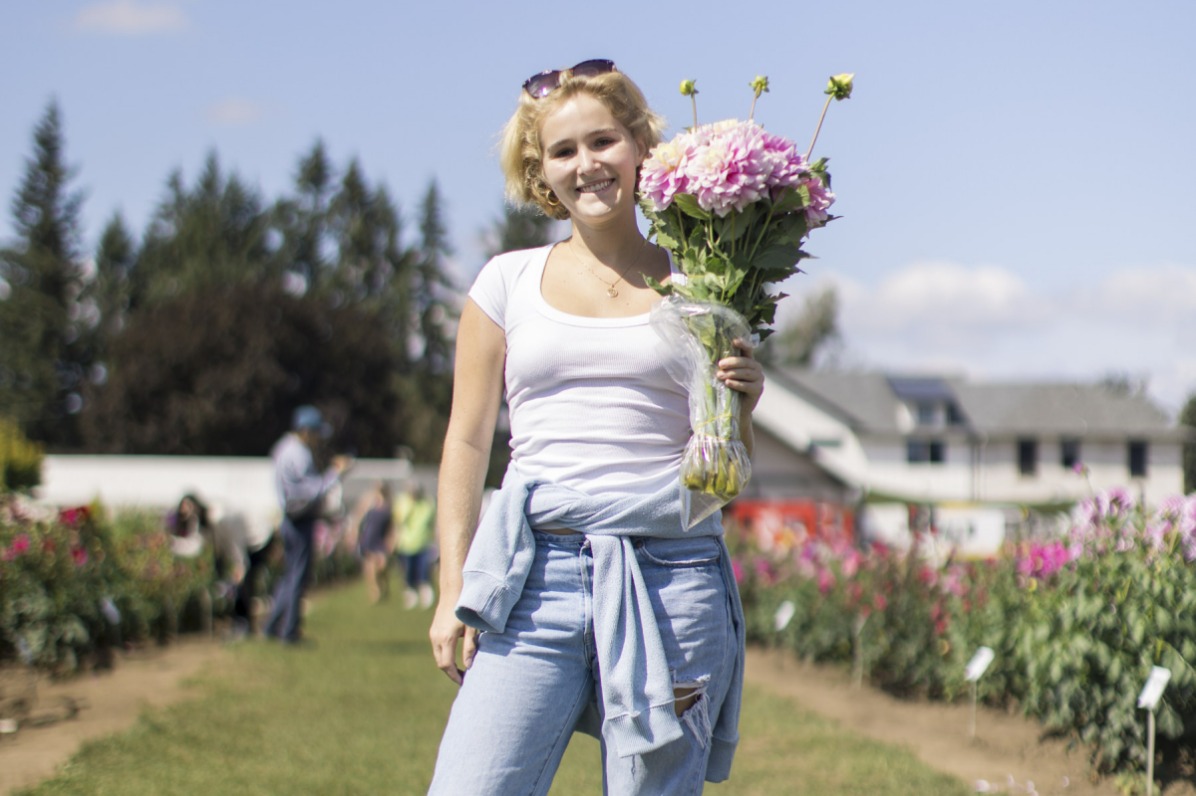 A person stands in a field of flowers holding a bouquet of pink flowers.