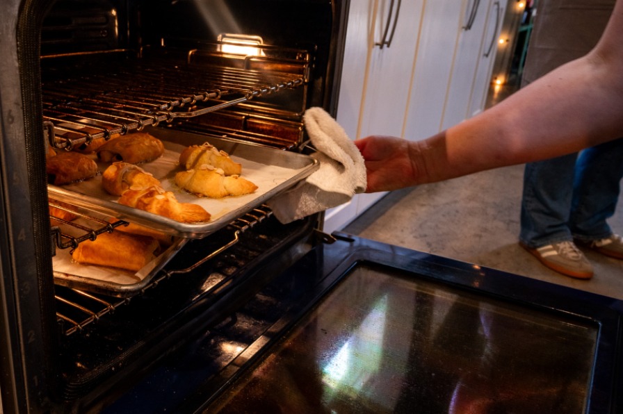 A hand pulls fresh baked goods out of an oven