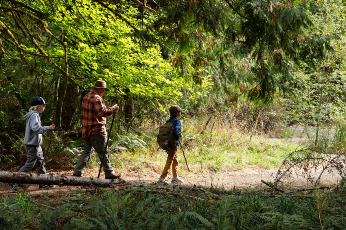 An older adult and two children on a path in the forest holding walking sticks