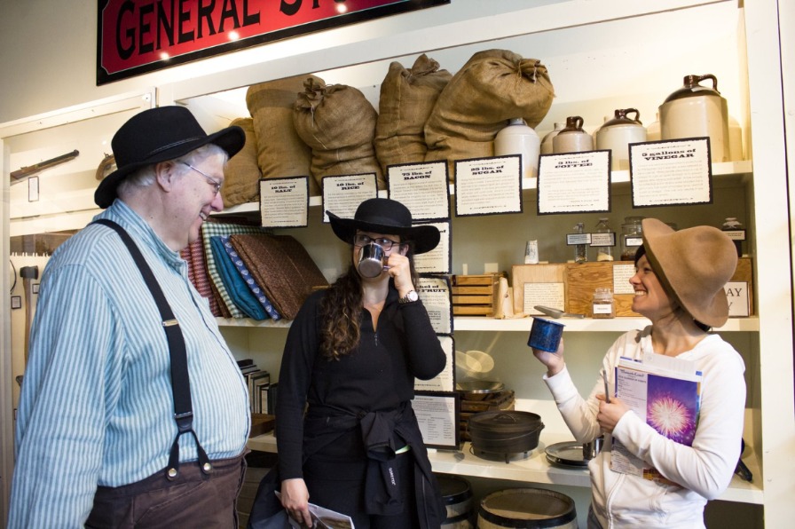 Three people in hats by a pioneer museum exhibit