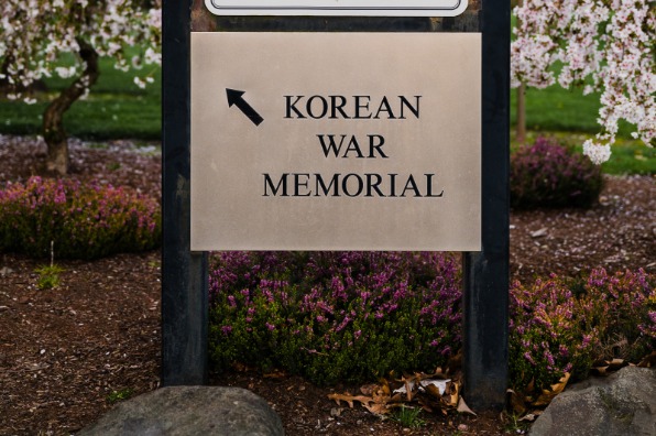 Sign at Town Center Park directing visitors to the Korean War Memorial, surrounded by blooming cherry blossom trees and landscaped gardens.