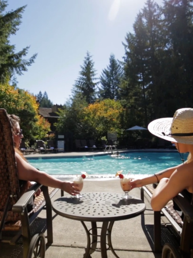 Two people relax on loungers with cocktails by a pool