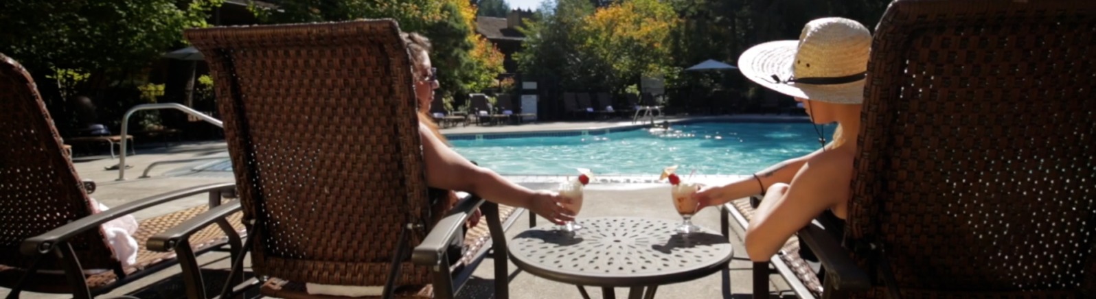 Two people relax on loungers with cocktails by a pool