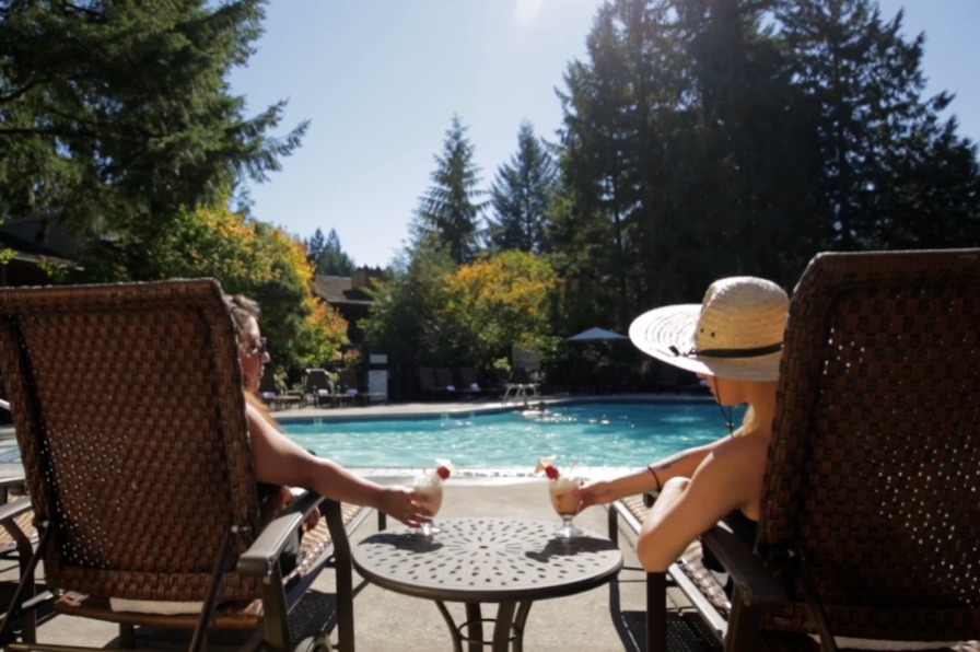 Two people relax on loungers with cocktails by a pool
