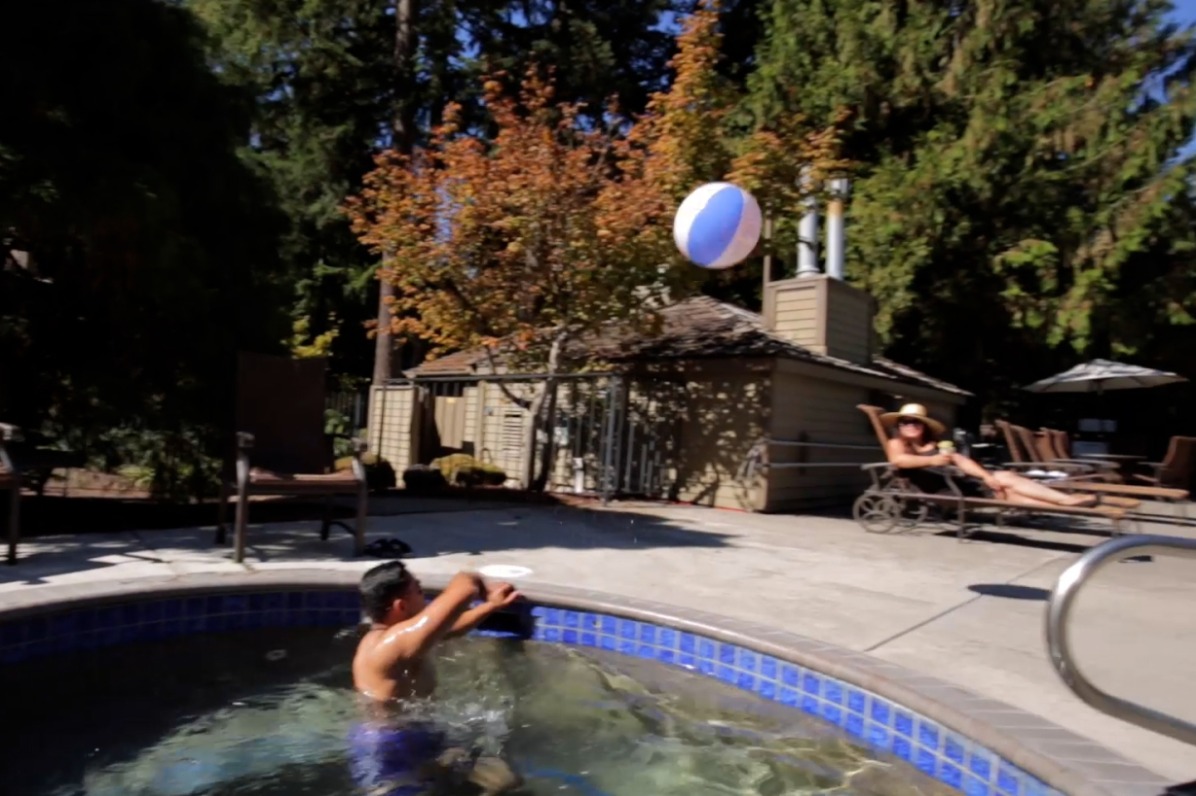 Person in a hot tub tosses a beach ball as someone in a lounger looks on