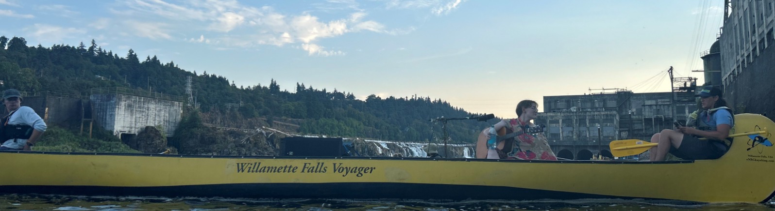 A musician sings any plays guitar in a long yellow canoe