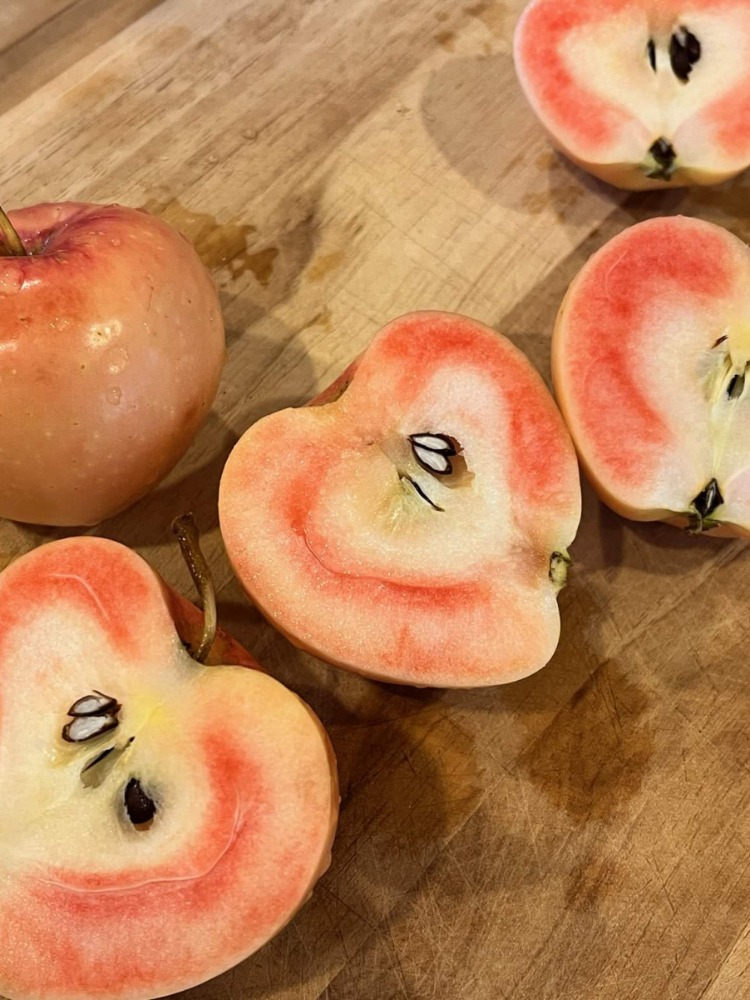 Pink and white apples are cut on a wood board