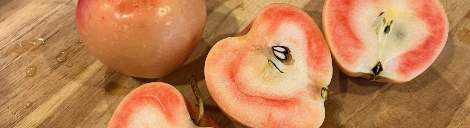 Pink and white apples are cut on a wood board