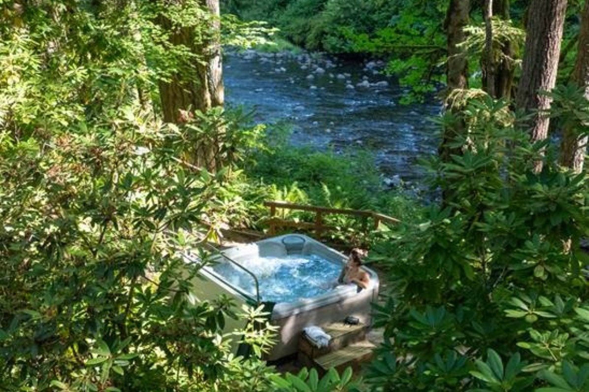 A person in a blue hot tub surrounded by green trees