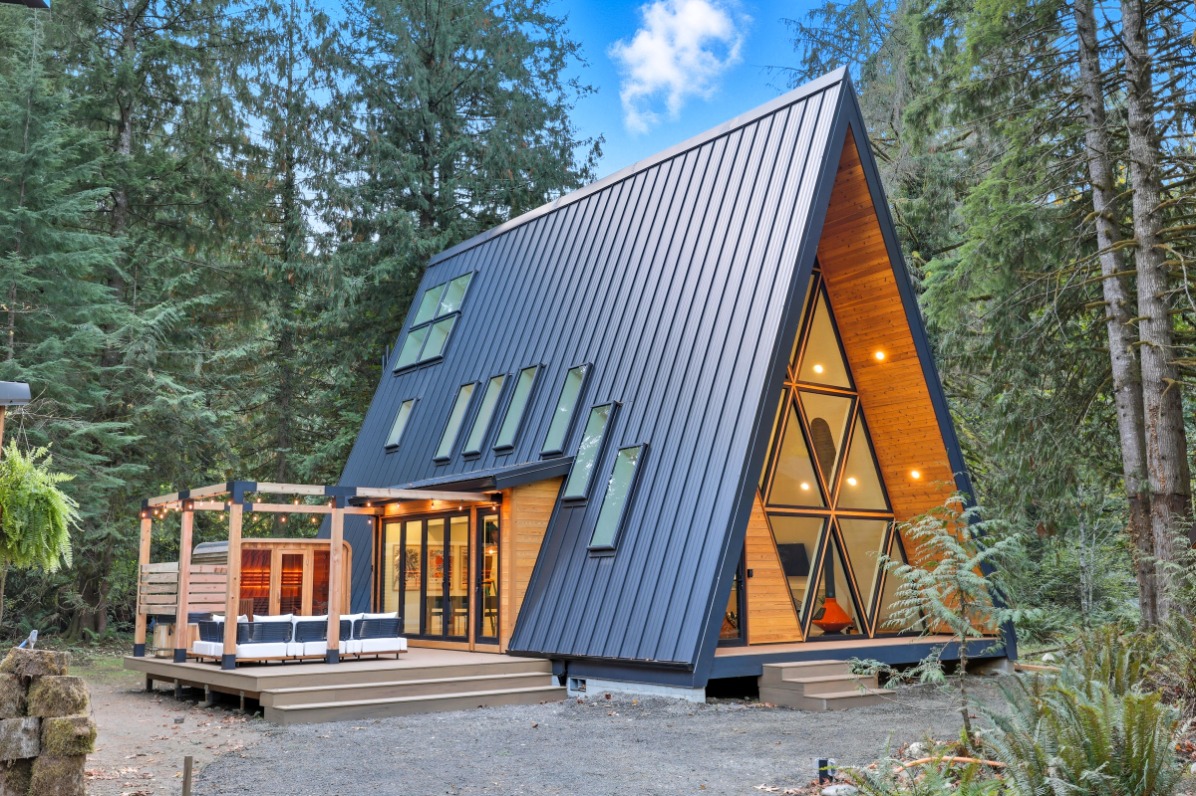 An aframe cabin with a metal roof surrounded by green trees.