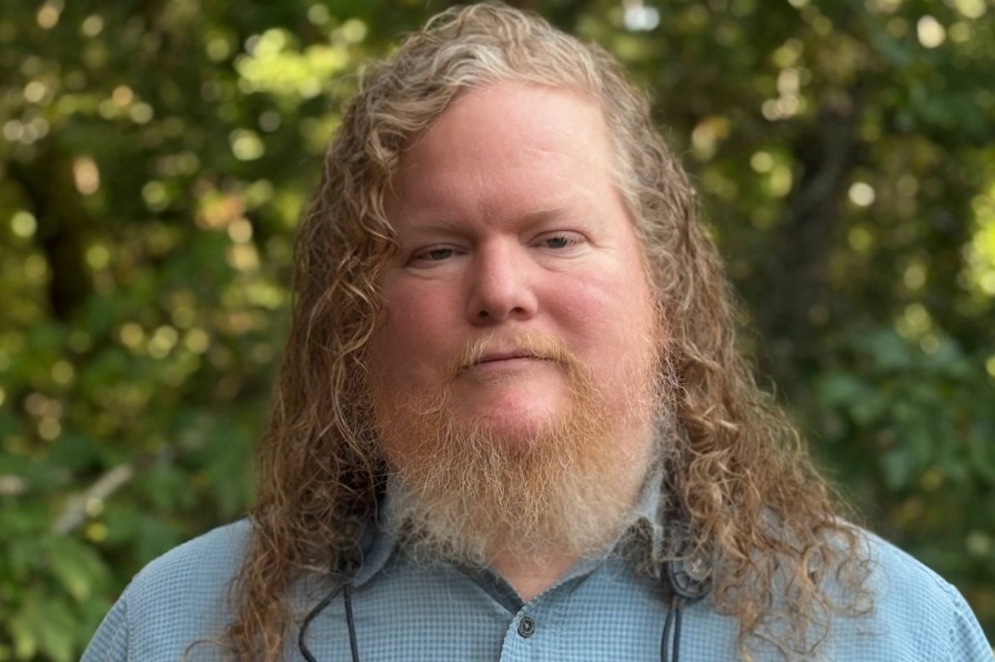 A person in a blue shirt stands against green trees.