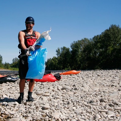 Two kayakers walk the Clackamas' riverbank with large trash bags which they are filling with trash left behind over summer.