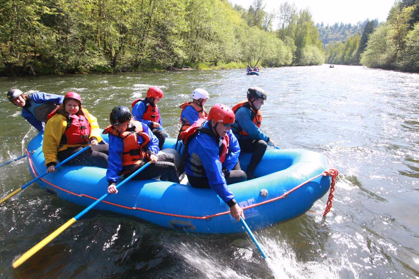 Six rafters and eNRG Kayaking guide in blue inflatable raft dip their oars in the Sandy River and begin their whitewater trip