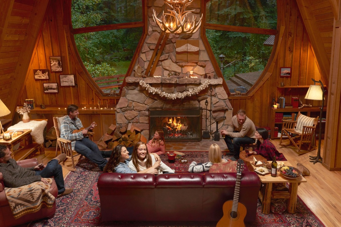 Families relax with hors doeuvres around stone fireplace in great room at Forrest Lodge as one plays music on his ukulele