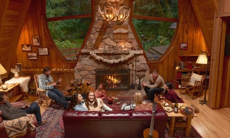 Families relax with hors doeuvres around stone fireplace in great room at Forrest Lodge as one plays music on his ukulele