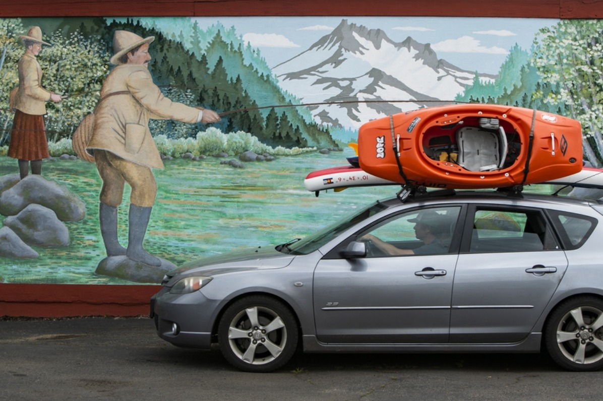 Car with kayaks on top drives by a mural of a man fishing in Estacada