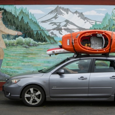 Car with kayaks on top drives by a mural of a man fishing in Estacada