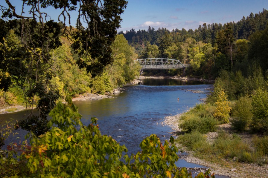 View of the Wild & Scenic Clackamas River with green trees, blue river and a bridge in distance in Oregon's Mount Hood Territory