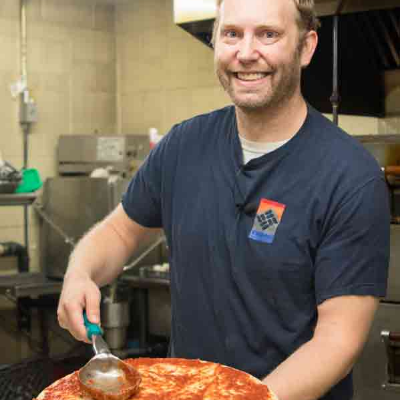 Ivy Bear Pizzeria owner Scott adding sauce to pizza dough 