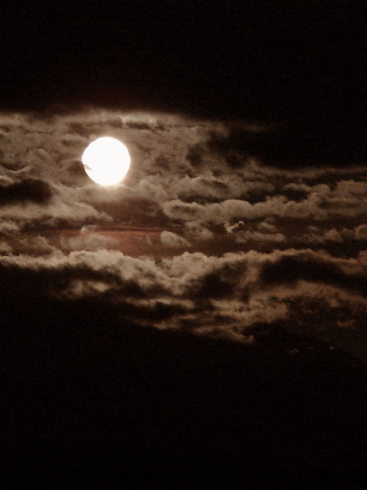 Full moon emerges revealing a sky full of clouds on a dark black spooky night