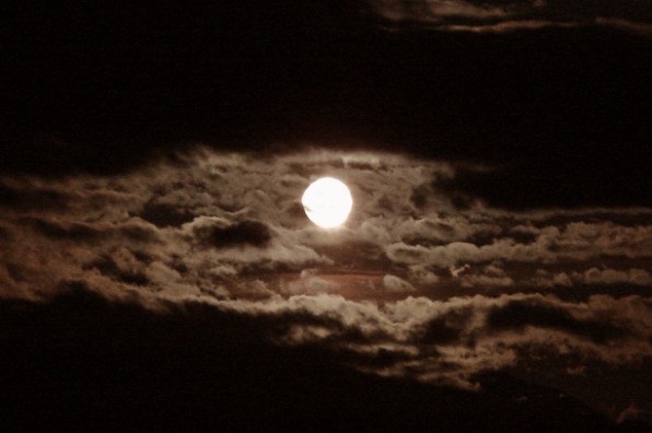 Full moon emerges revealing a sky full of clouds on a dark black spooky night